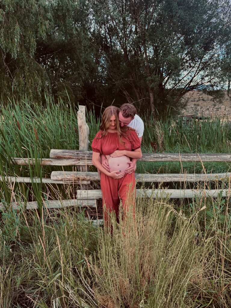 man and woman standing in field taking pregnancy picture 